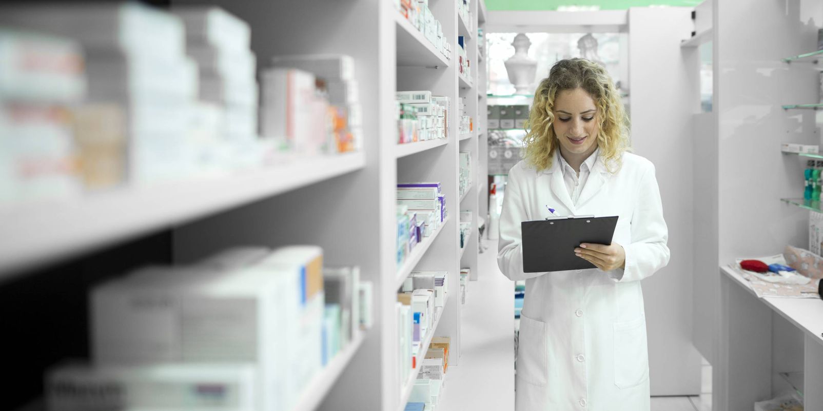 Pharmacist in white uniform walking by the shelf with medicines and checking inventory.