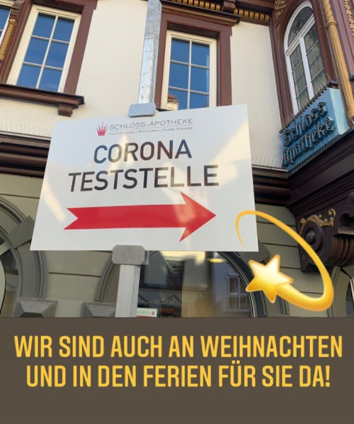 ein Bild des Schildes der Teststelle, im Hintergrund die Schlossapotheke Bildtext: Wir sind auch an Weihnachten und in den Ferien für Sie da!