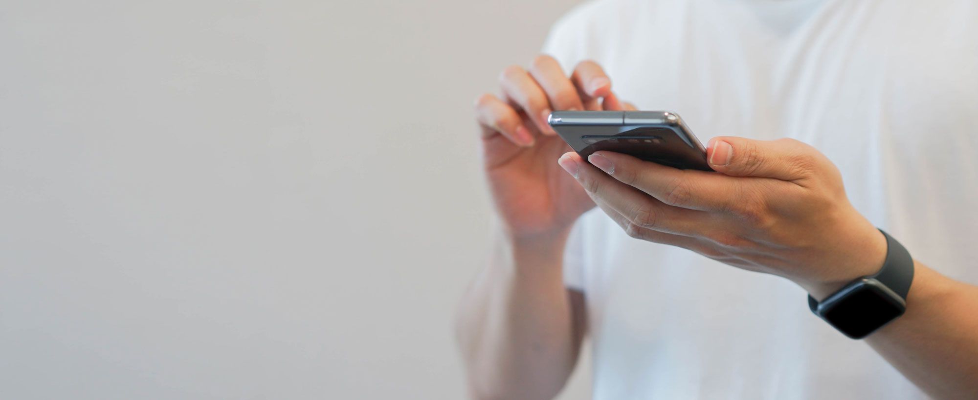 Zwei Hände, in der einen Hand ein Smartphone, die andere Hand will etwas antippen