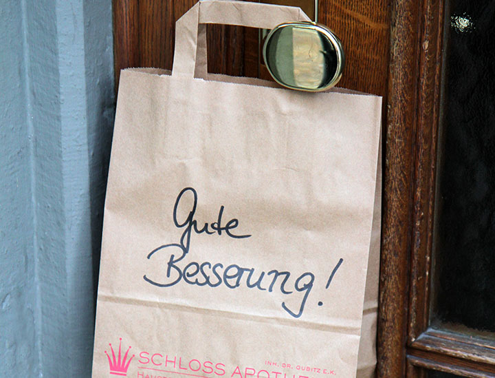 Eine Papiertüte hängt an einem goldenen Türknauf mit Aufschrift "Gute Besserung!"