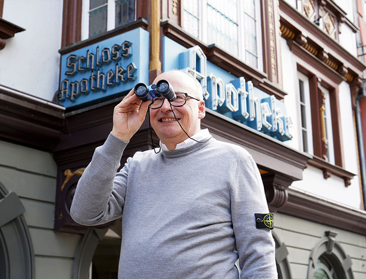Dr. Gubitz mit Fernglas vor der Apotheke