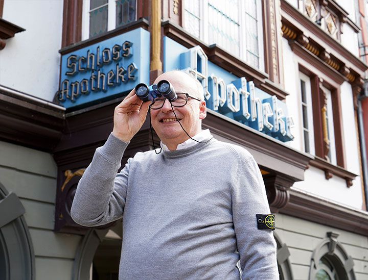 Dr. Gubitz mit Fernglas vor der Apotheke