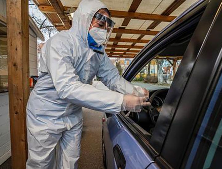 ein Testmitarbeiter in Schutzkleidung steht an einem geöffneten Autofenster