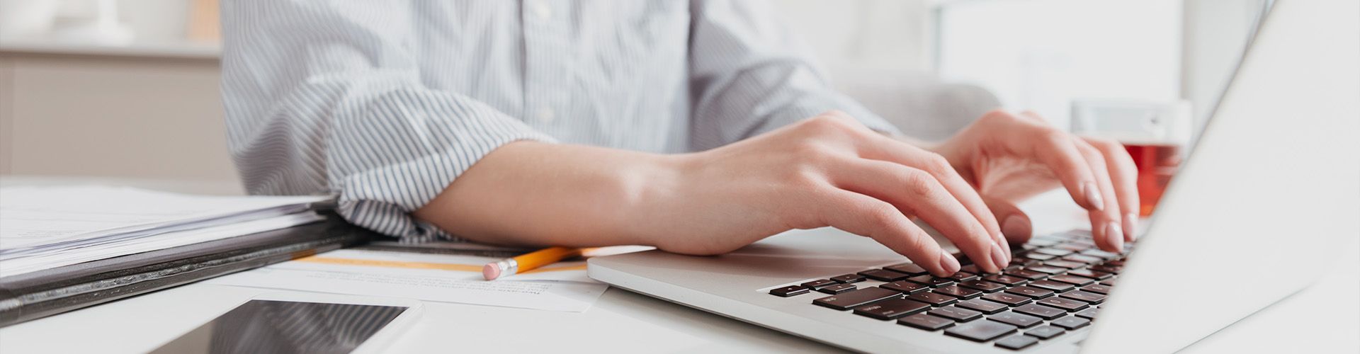 eine Person sitzt vor einem Laptop, die Hände liegen auf der Tastatur