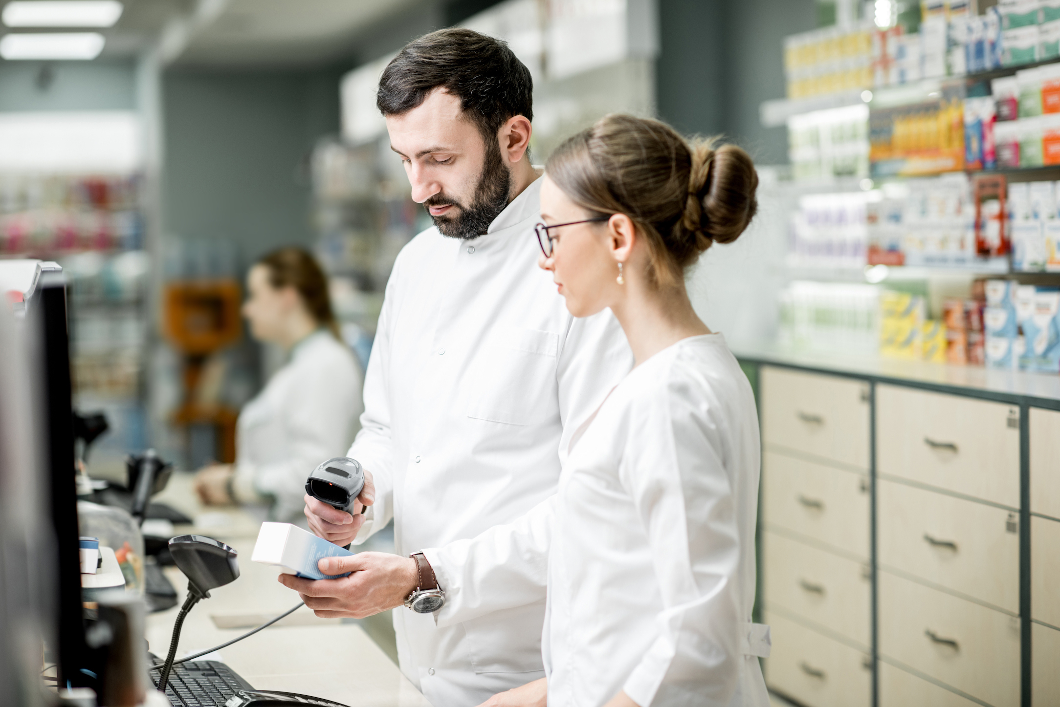 zwei Personen stehen an einer Kasse, die linke Person scannt ein Produkt ab