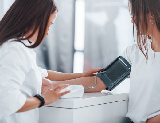 eine Person misst der gegenübersitzenden Person mit einer Oberarmmanschette den Blutdruck