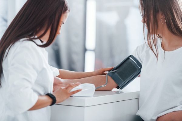 eine Person misst der gegenübersitzenden Person mit einer Oberarmmanschette den Blutdruck