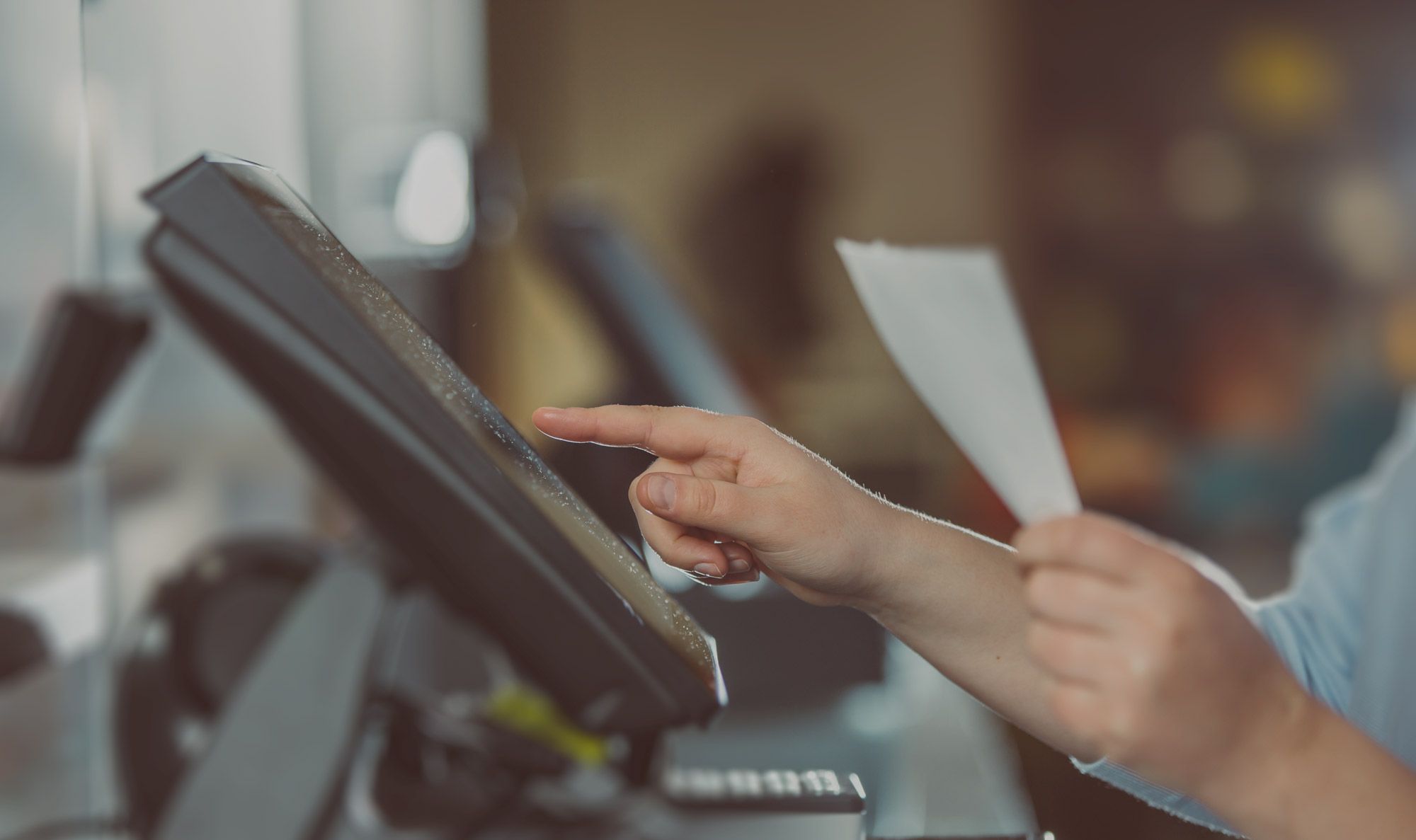 Eine Person hält einen Zettel in der Hand und tippt etwas auf einem Bildschirm an