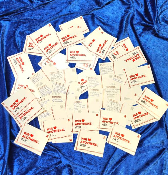ein Haufen Karten mit "Wir lieben Apotheke, weil..."-Aufdruck auf blauem Stoff