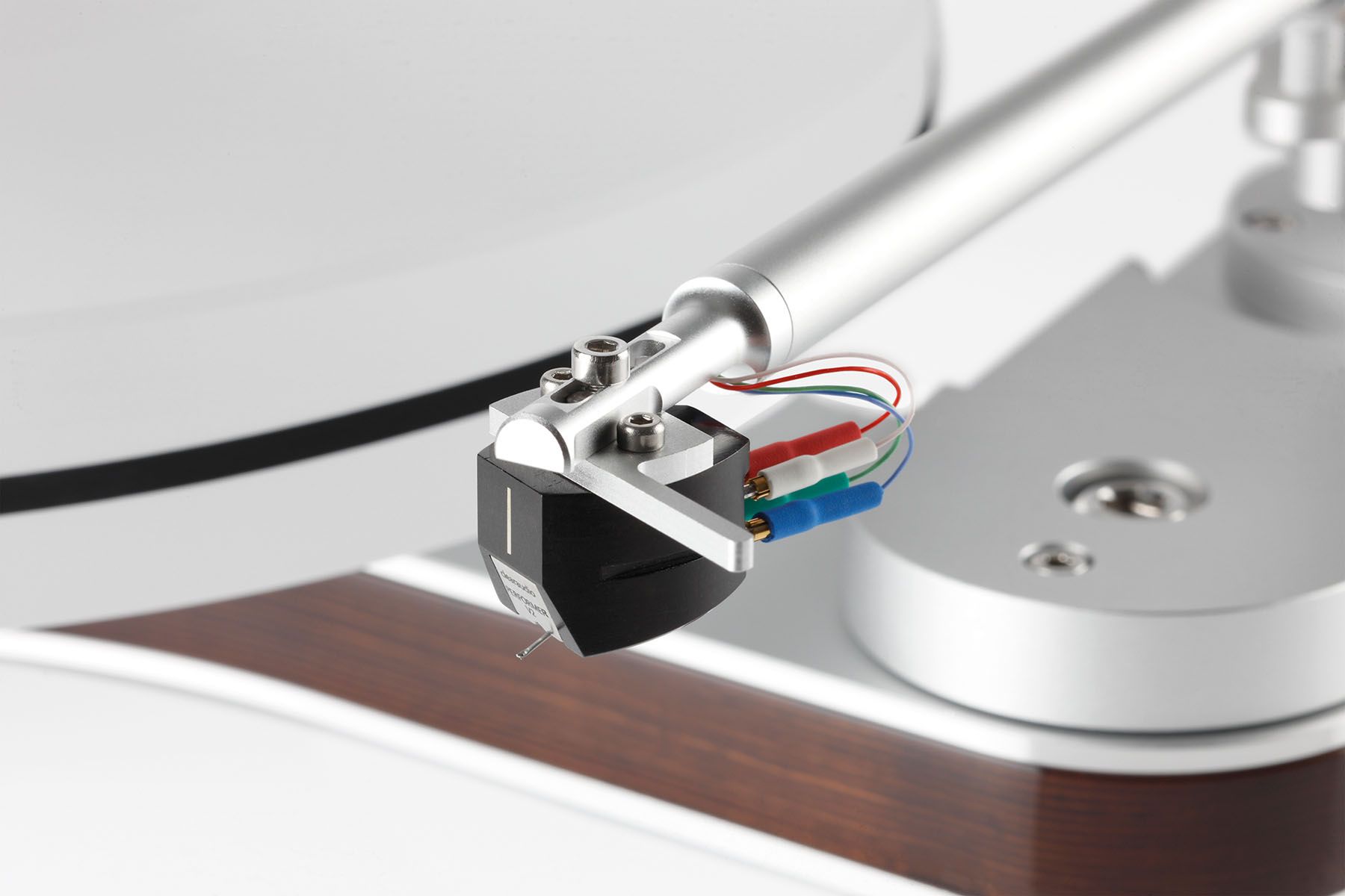 Makroaufnahme eines Clearaudio Moving-Magnet-Tonabnehmers an einem silbernen Tonarm über dem Plattenteller des Innovation Basic Wood.