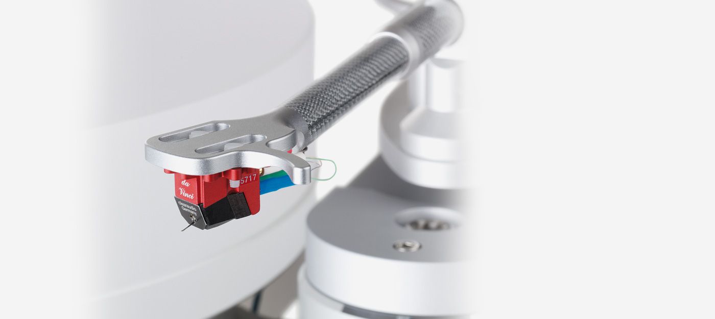 Nahaufnahme des roten Clearaudio da Vinci V2 MC-Tonabnehmers, präzise montiert am silbernen Headshell eines Carbon-Tonarms über einem hellen Plattenteller.