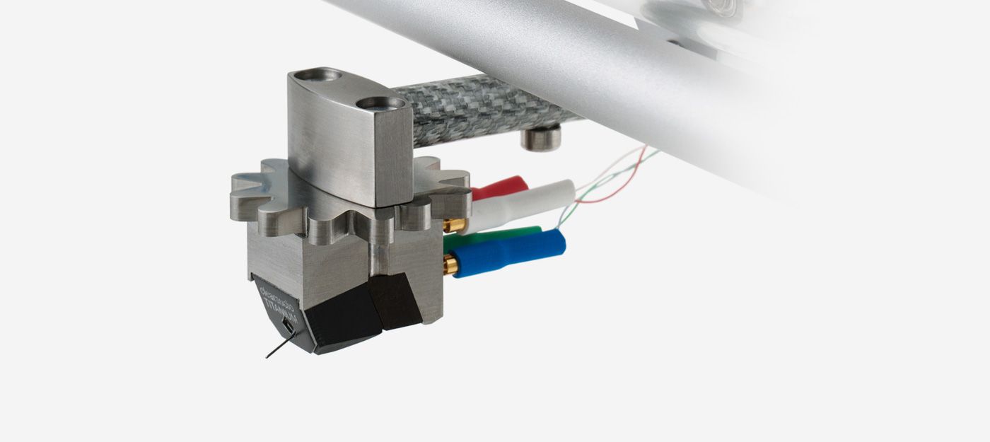 Nahaufnahme des Clearaudio Titanium V2.1 Moving-Coil-Tonabnehmers mit charakteristischem, zahnradförmigen Titankörper, montiert an einem Carbon-Tonarmrohr mit farbigen Anschlusskabeln.