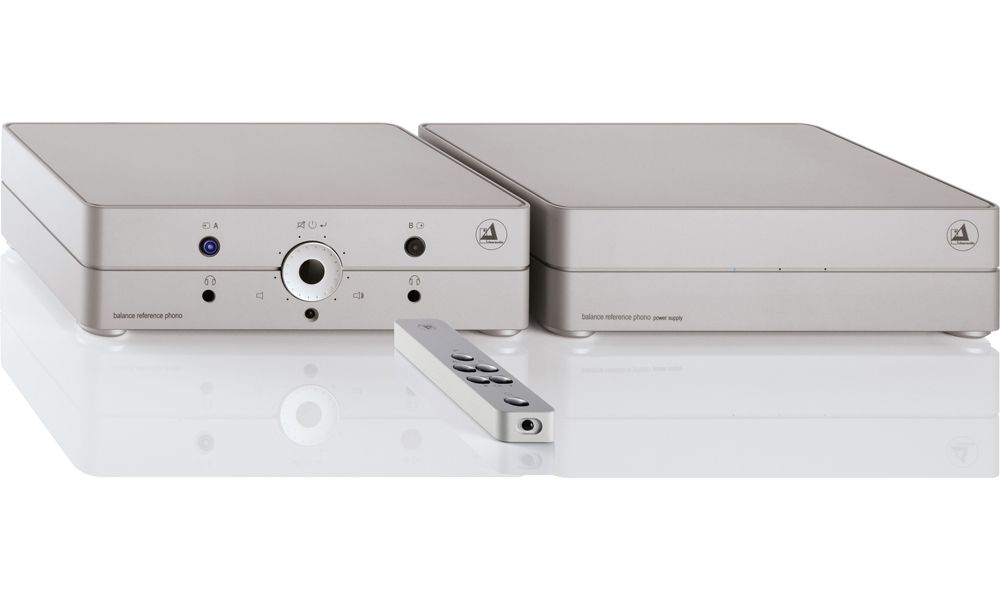 Silberne Ausführung der zwei clearaudio Audiokomponenten mit zentralem Bedienelement und Anschlüssen auf der Frontseite, davor liegend eine schlanke, minimalistische Fernbedienung aus Metall auf weißem Untergrund.