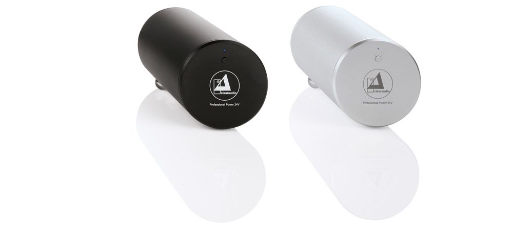 Zwei zylindrische clearaudio Professional Power Netzteile – eine Variante in Schwarz und eine in Silber – nebeneinander auf einer weißen, spiegelnden Oberfläche.