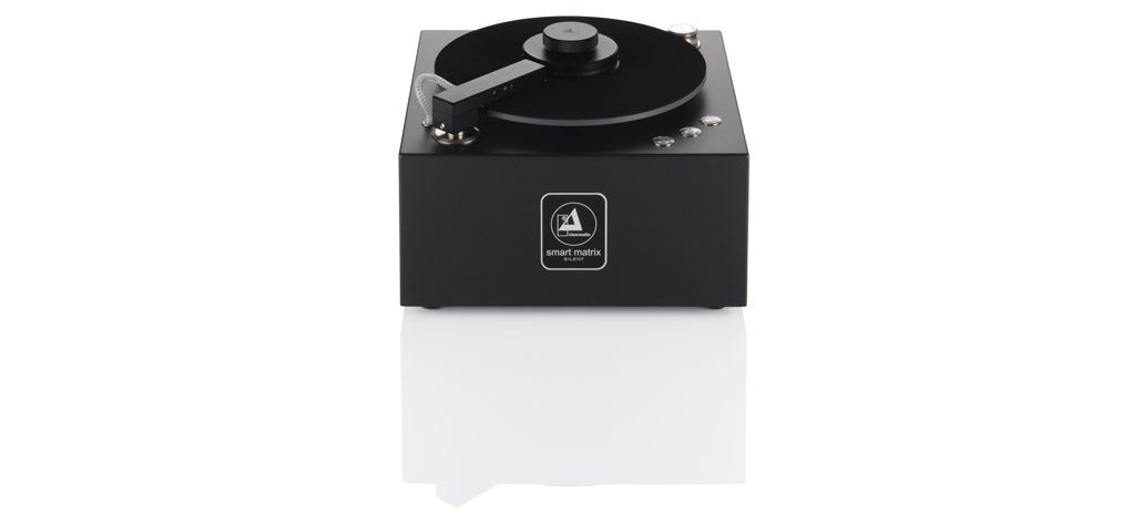 Frontansicht der kompakten, würfelförmigen clearaudio smart matrix SILENT Schallplattenwaschmaschine in Schwarz mit aufgelegter Vinyl-Schallplatte auf weißem, spiegelndem Untergrund.