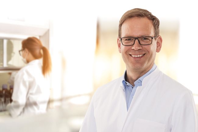 Porträt Ralf König im Labor mit arbeitender Mitarbeiterin im Hintergrund