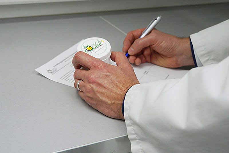 Apotheker kontrolliert die hergestellte Salbe und gibt diese frei. Hände halten eine Kruke und einen Kugelschreiber