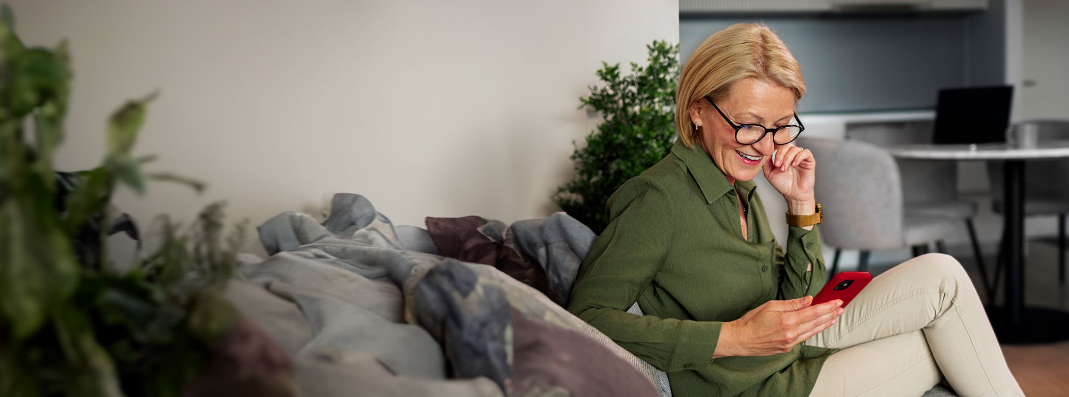 ältere Frau sitzt auf der Couch und schaut auf ihr Handy