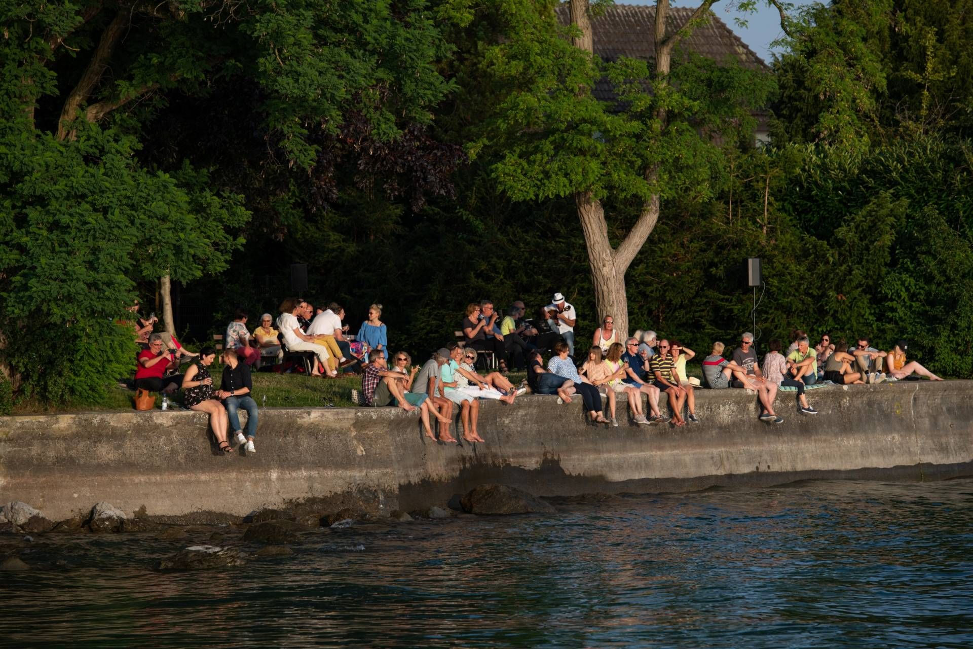 Musik und Wein am See, Leute sitzen am Seeufer