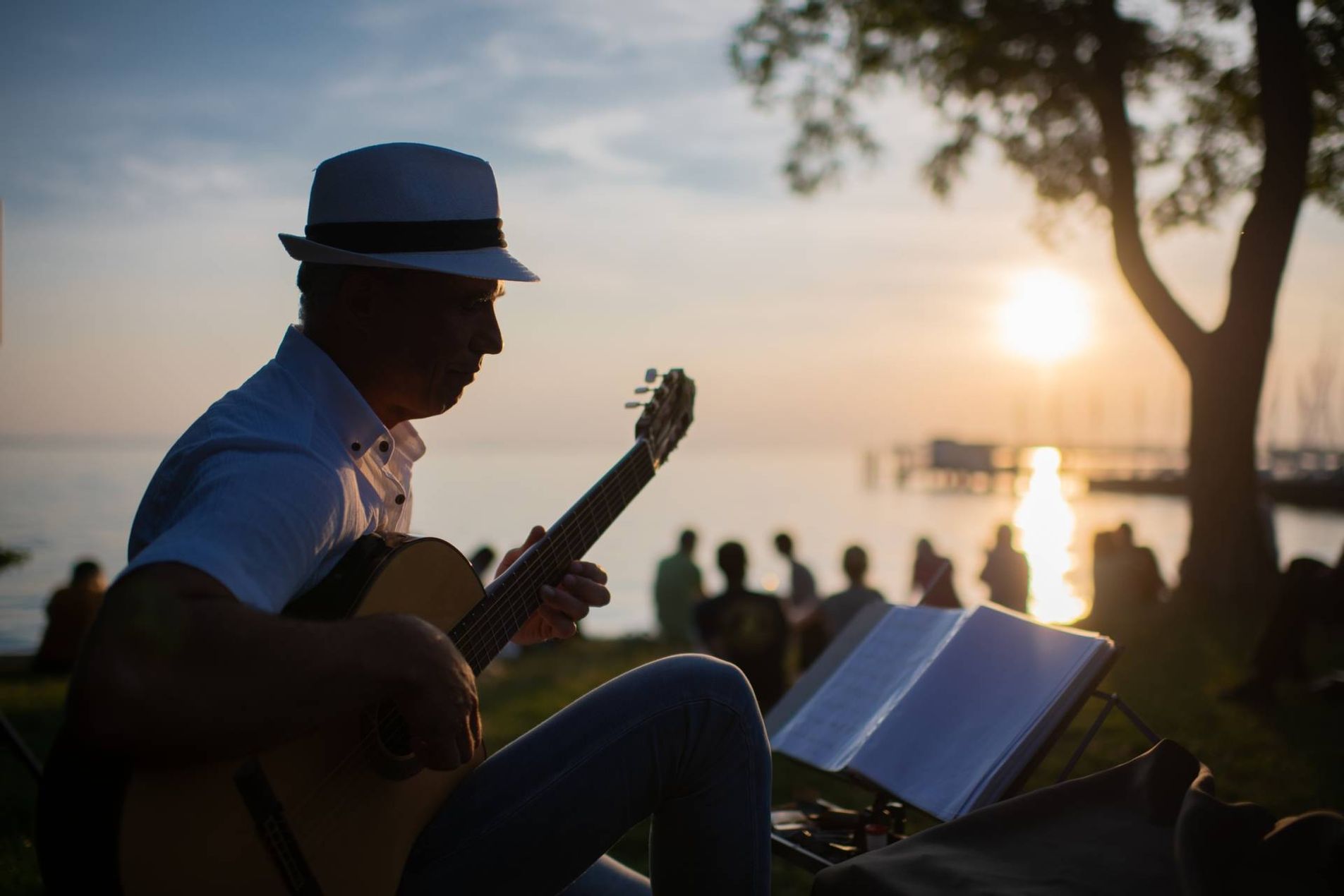 Mann mit Gitarre und Hut am Seeufer, Sonnenuntergang