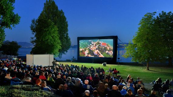 Open Air Kino im Freibad Aquamarin. Leinwand auf der Liegewiese. Im Hintergrund der Bodensee und die Bergwelt.