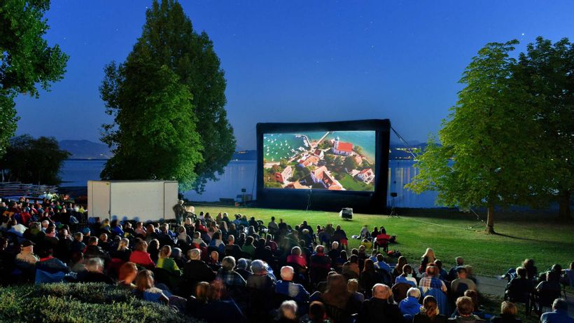 Open Air Kino im Freibad Aquamarin. Leinwand auf der Liegewiese. Im Hintergrund der Bodensee und die Bergwelt.