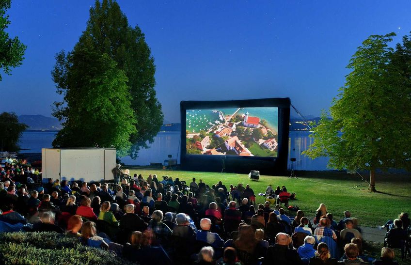 Open Air Kino im Freibad Aquamarin. Leinwand auf der Liegewiese. Im Hintergrund der Bodensee und die Bergwelt.