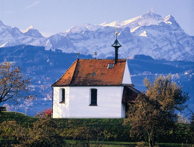 Antoniuskapelle in Selmnau. Im Vordergrund sind Felder zu sehen. Im Hintergrund die verschneite Bergwelt.