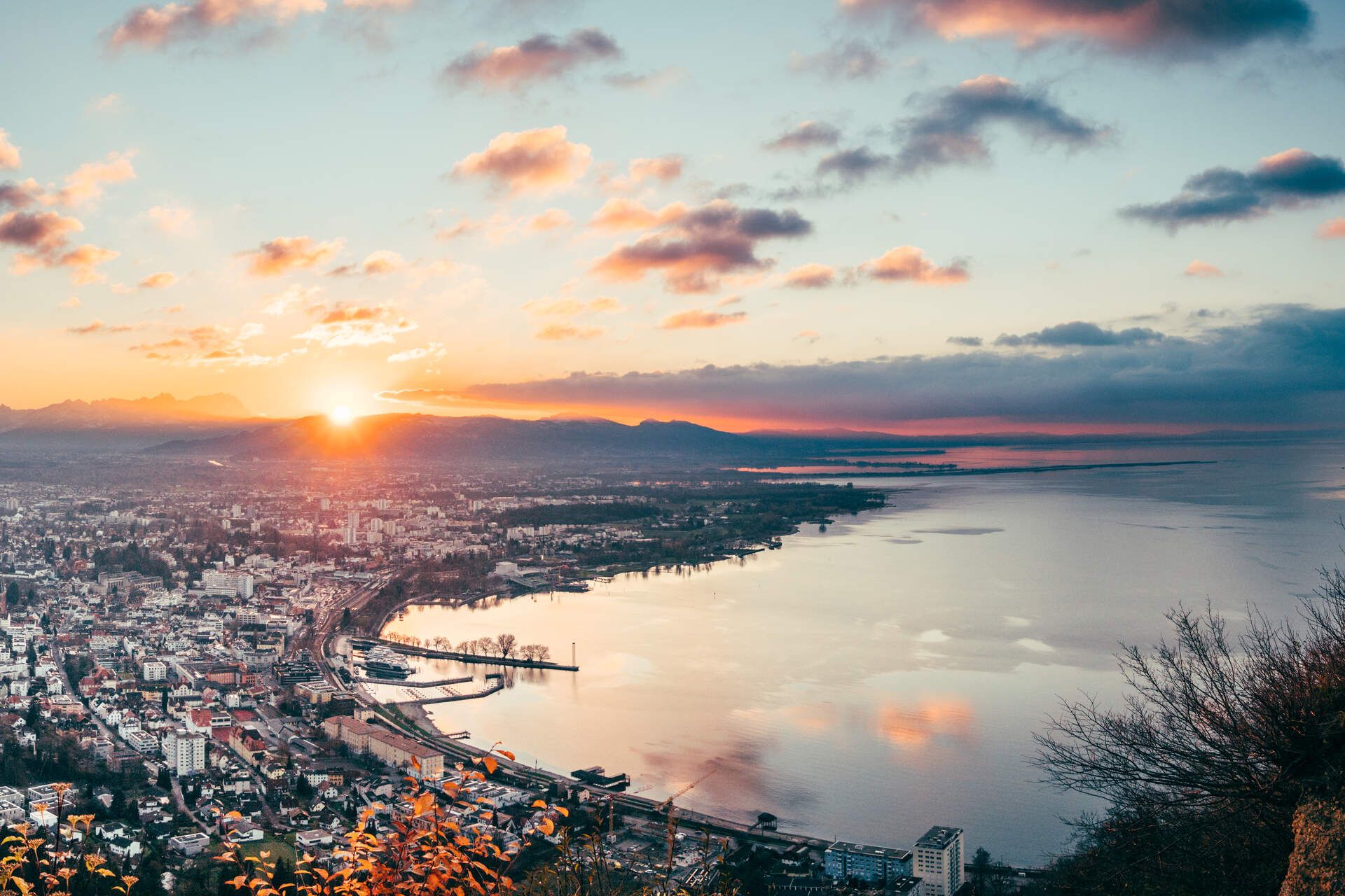 Lufttbild von einem teil des Bodensees. Im Hintergrund sieht man die Berge und die Sonne geht unter.