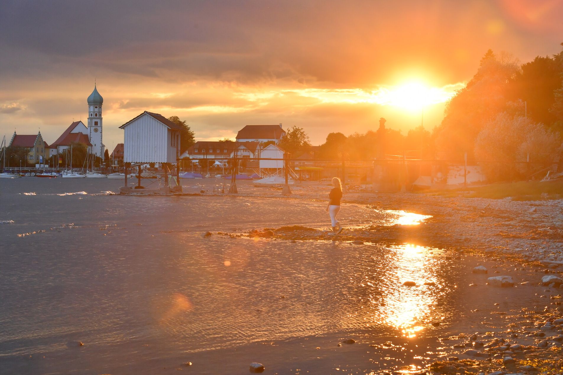 Die Halbinsel in Wasserburg umringt von einem Sonnenuntergang. Eine Frau genießt dort die Aussicht.