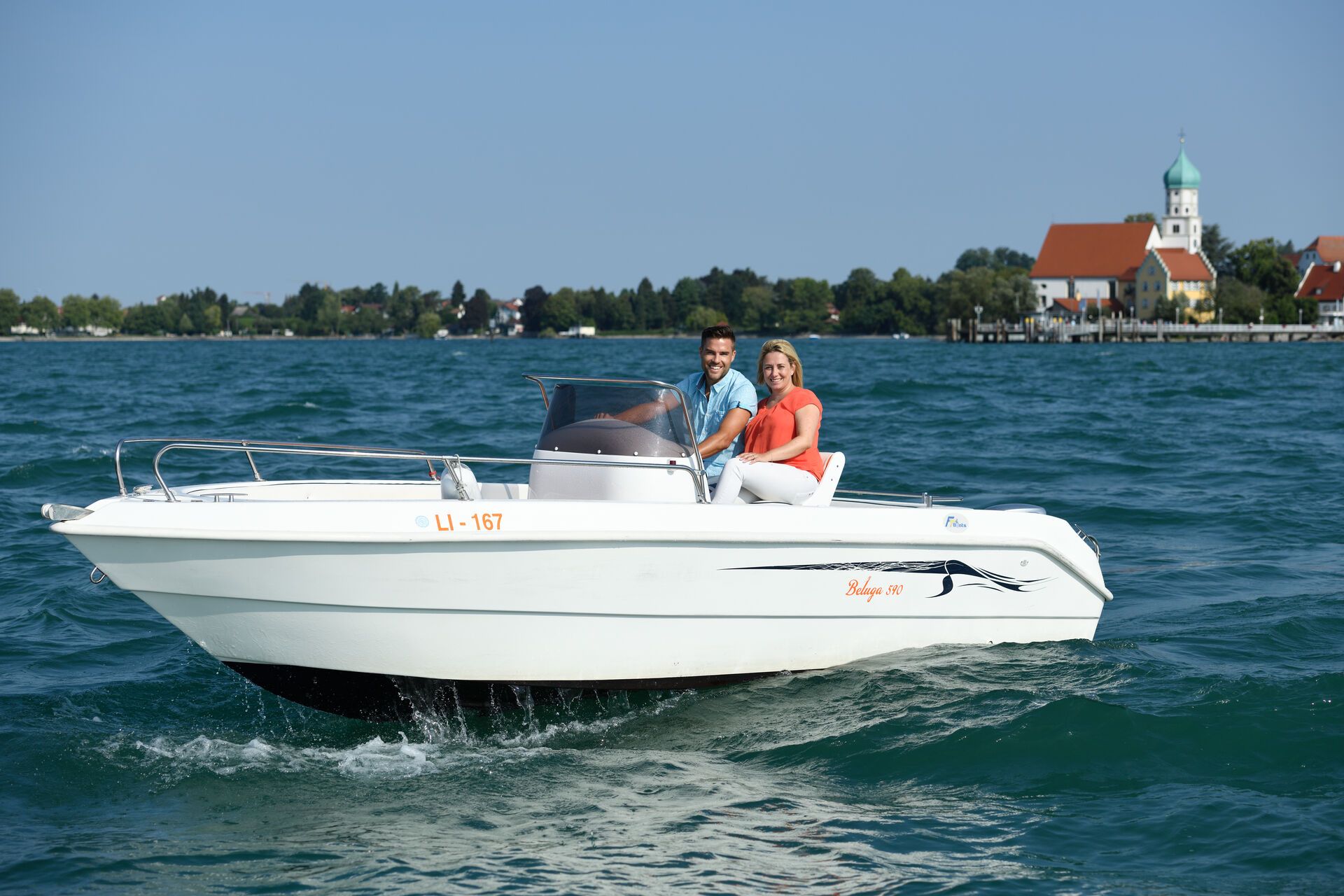 Ein Mann und eine Frau auf einem Motorboot vor der Halbinsel in Wasserburg. Umringt vom See.