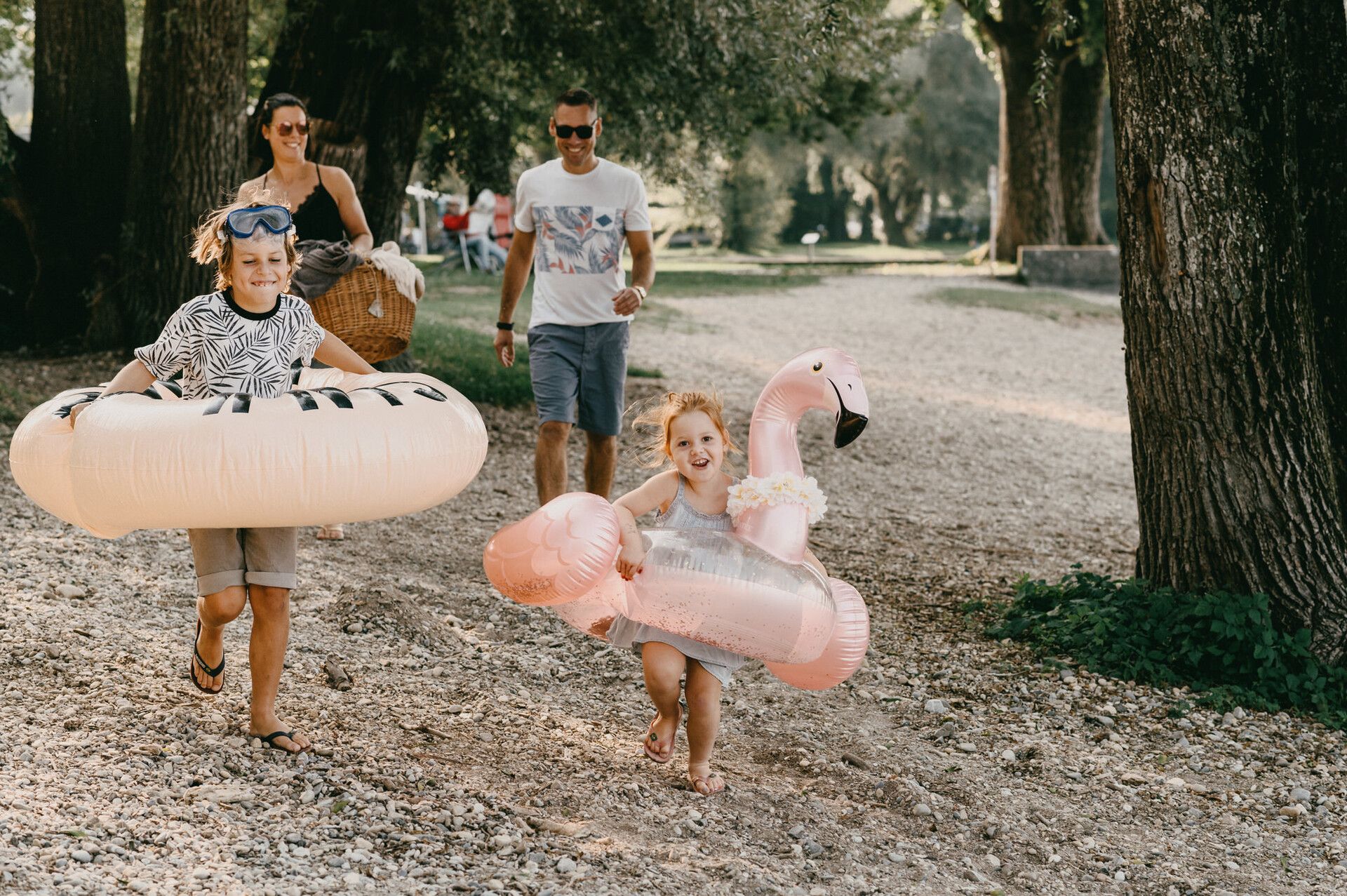 Eine Familie mit zwei Kindern auf dem Weg zum See. Die Kinder haben jeweils ein Schwimmreifen dabei.