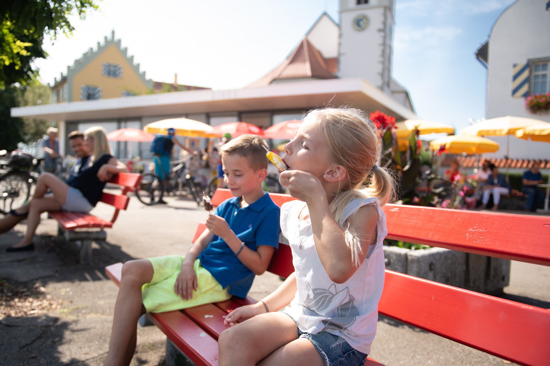 Auf der Halbinsel in Wasserburg sitzen zwei Kinder auf einer Bank und essen ihr Eis.