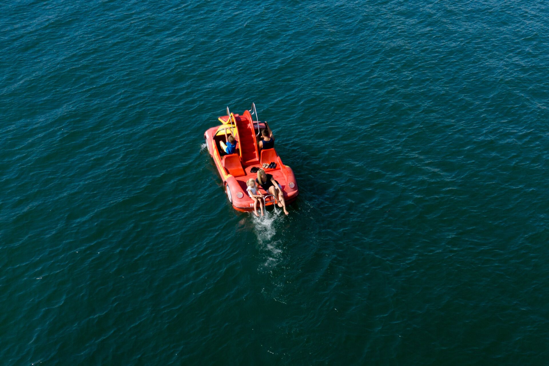 Luftaufnahme von einer Familie mit zwei Kindern auf einem Tretboot umringt vom Bodensee.