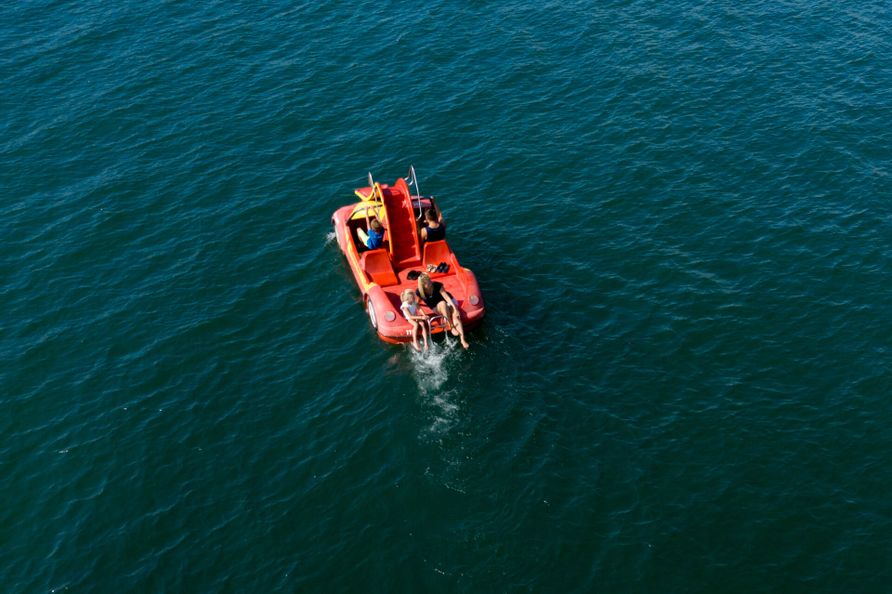 Luftaufnahme von einer Familie mit zwei Kindern auf einem Tretboot umringt vom Bodensee.