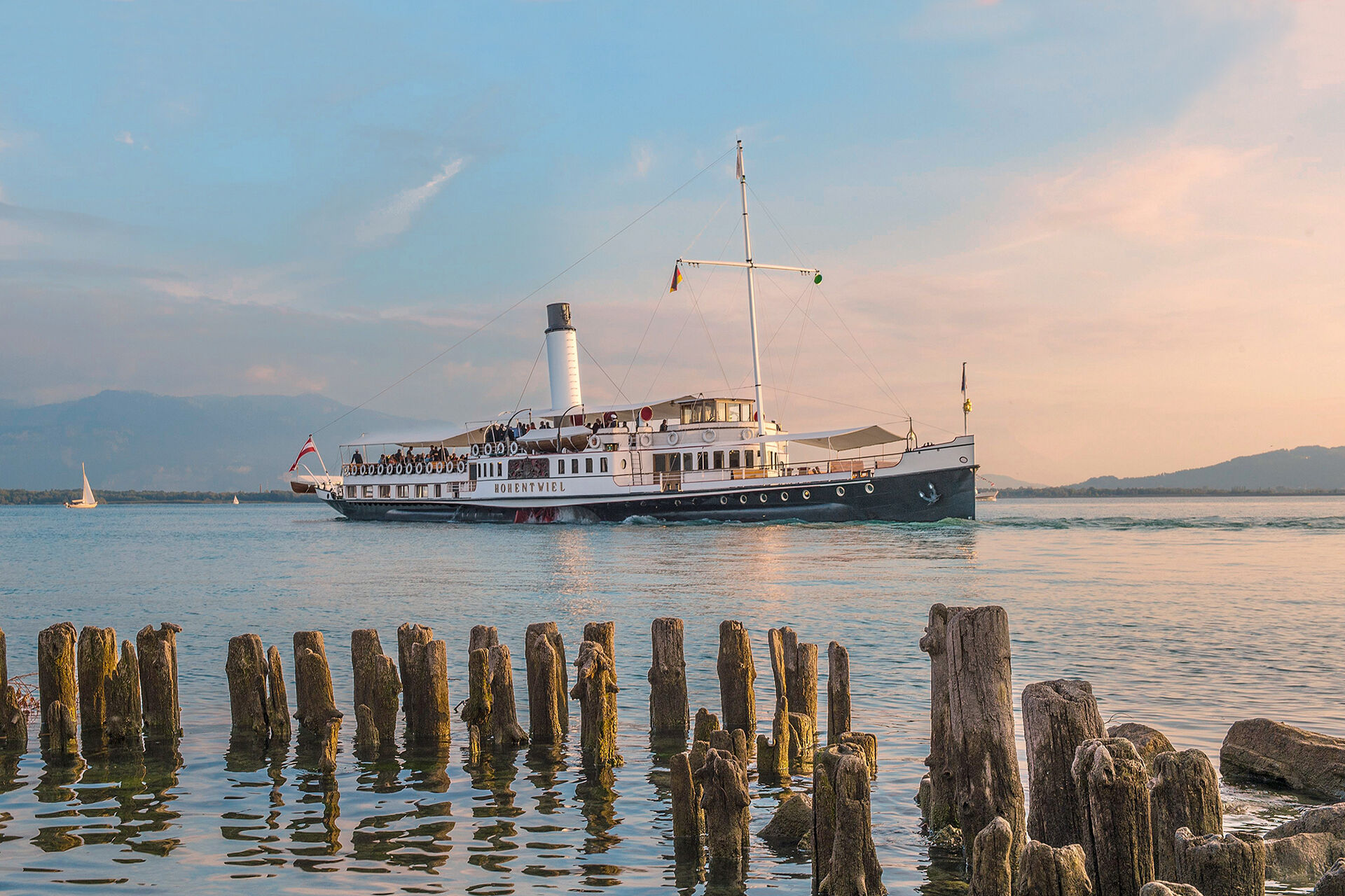 Das Dampfschiff Hohentwiel auf dem Bodensee. Im Hintergrund verfärbte Wolken vom Sonnenuntergang zu sehen sowie die Bergwelt.