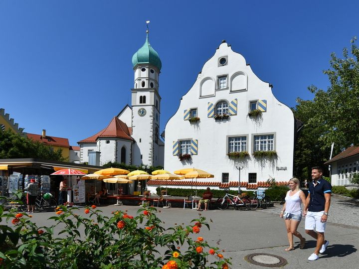 Ein Pärchen flaniert auf der Halbinsel in Wasserburg. Im Hintergrund ist die Kirch St. Georg, der Kiosk und das Museum im Malhaus zu sehen.