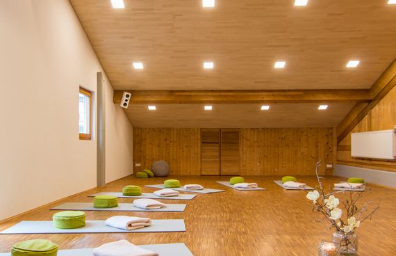 Ein Yoga-Raum mit Yoga Matten in der Mitte steht eine Kerze und eine Vase mit Blumen.
