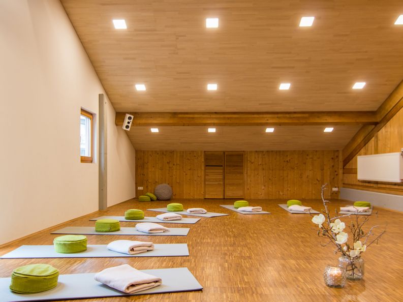 Ein Yoga-Raum mit Yoga Matten in der Mitte steht eine Kerze und eine Vase mit Blumen.