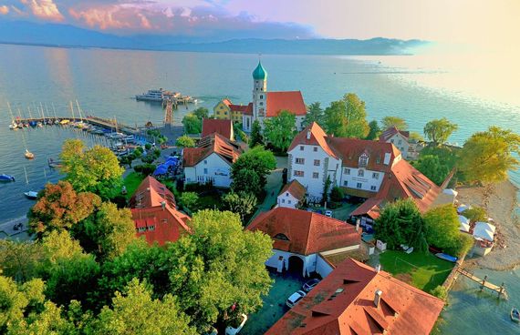 Luftaufnahme der Halbinsel in Wasserburg. Umringt vom Bodensee, im Hintergrund ist die Bergwelt zu sehen.
