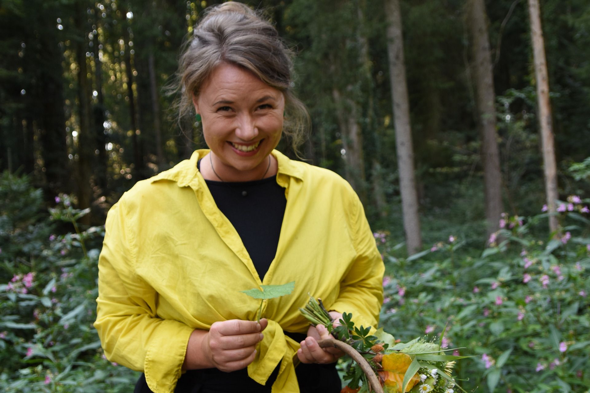 Kräutertour mit Dajana Krüger von Grün sein. Im Hintergrund ist ein Wald zu sehen,