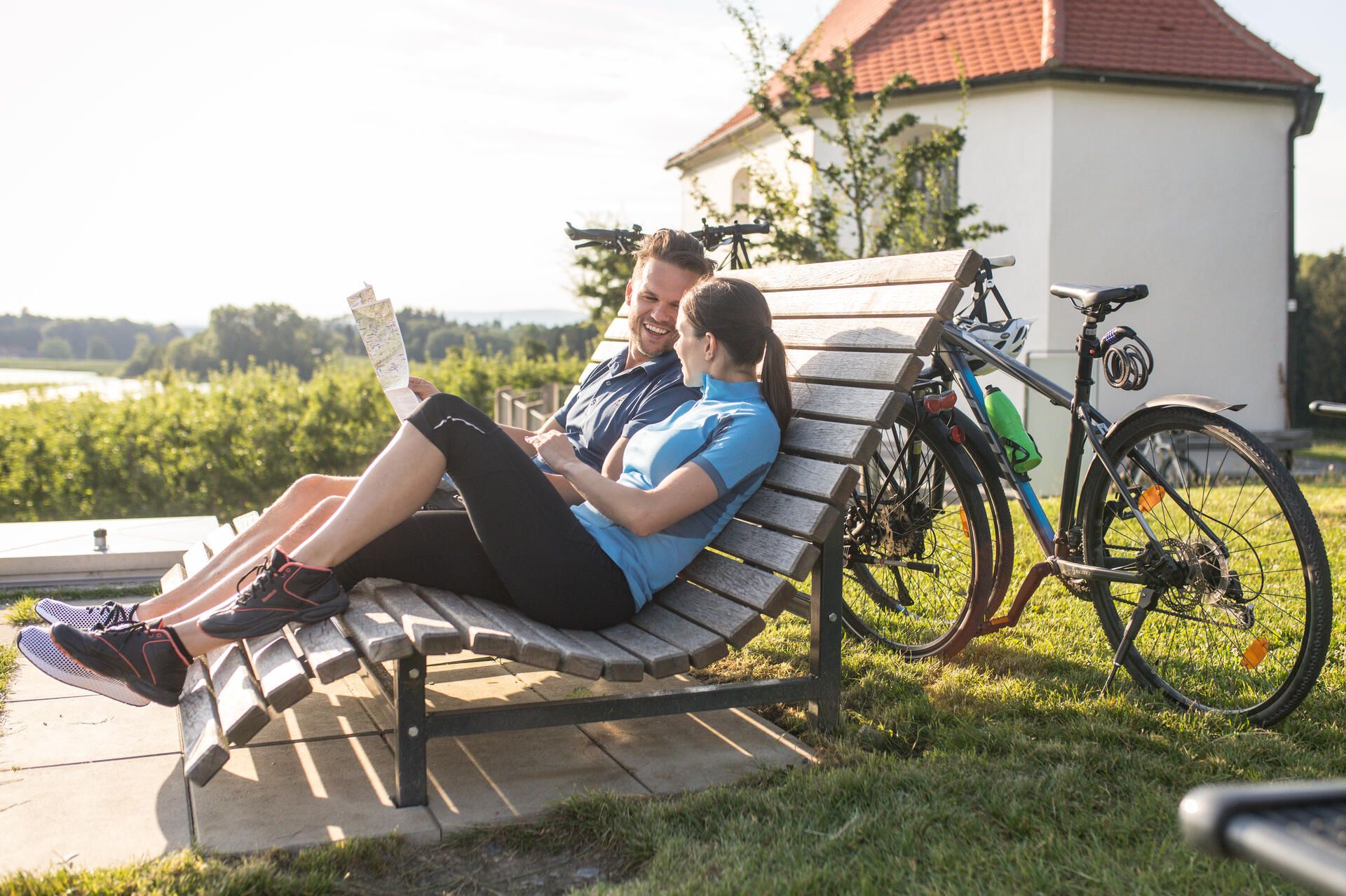 Ein Pärchen sitzt auf einer Bank an der Antoniuskapelle in Selmnau und hält eine Rad karte in der Hand. Die Fahrräder lehnen an der Bank an.