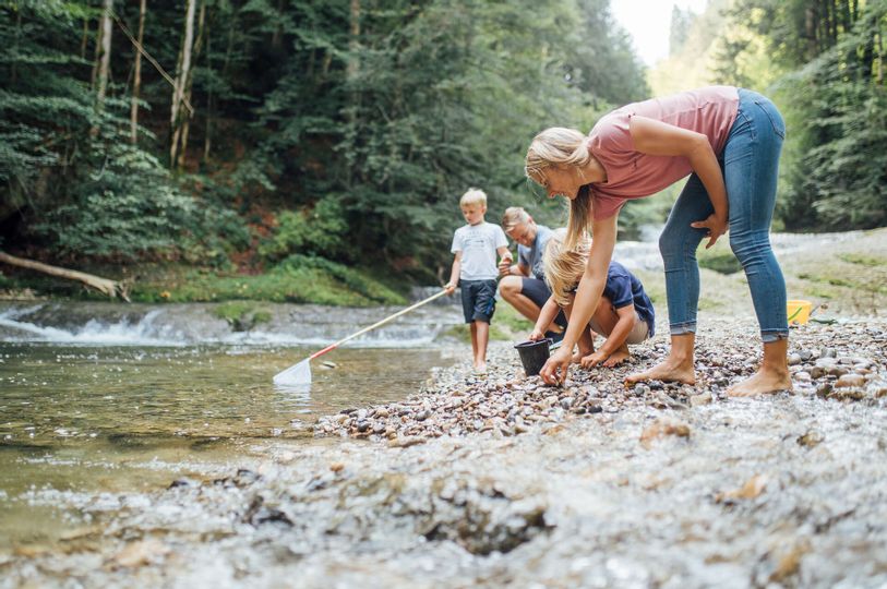 Eine Familie spielt an einem Fluss der durch ein Wald führt.