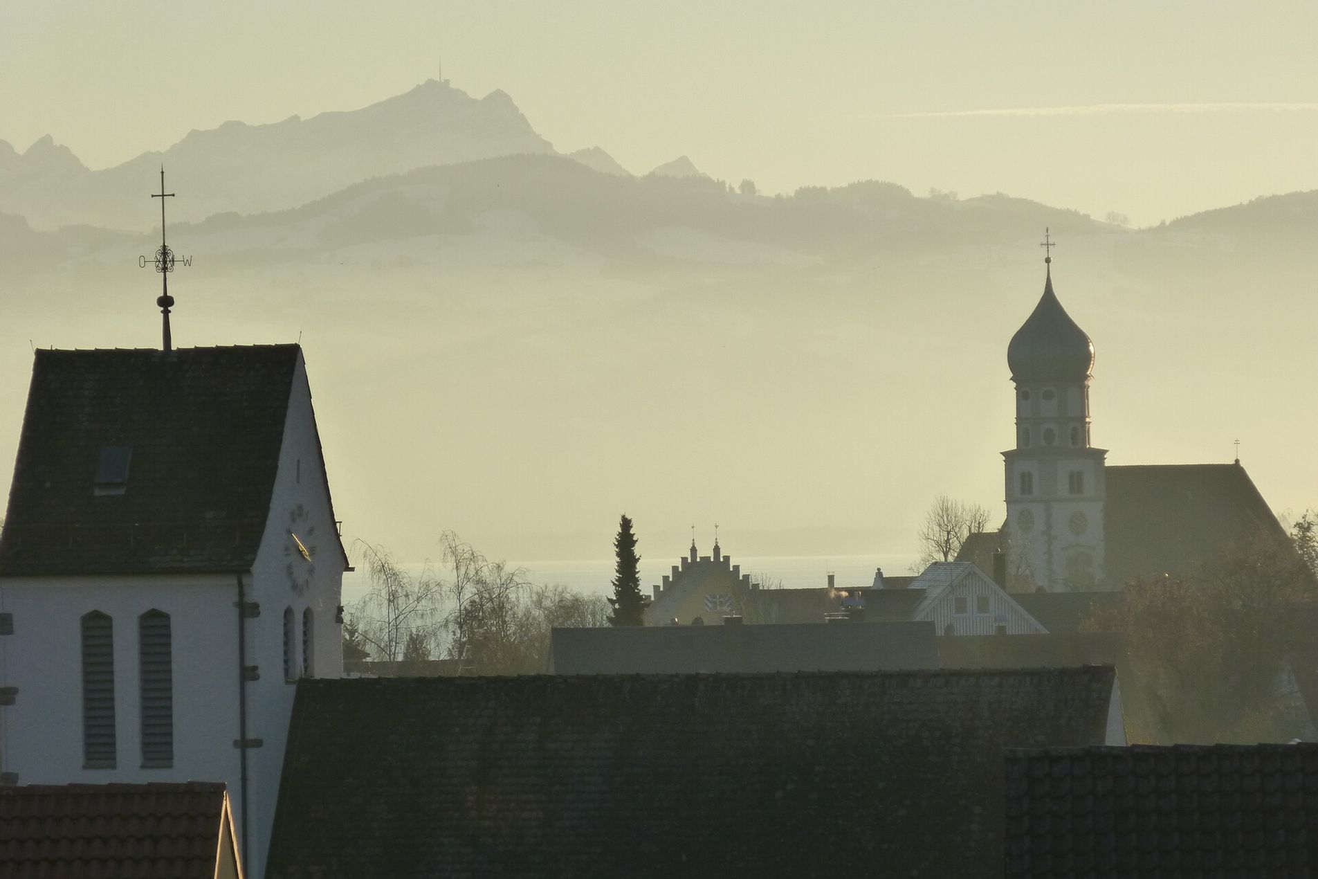 Kirche in Wasserburg umringt von Nebel, im Hintergrund ist leicht die Bergwelt zu sehen.