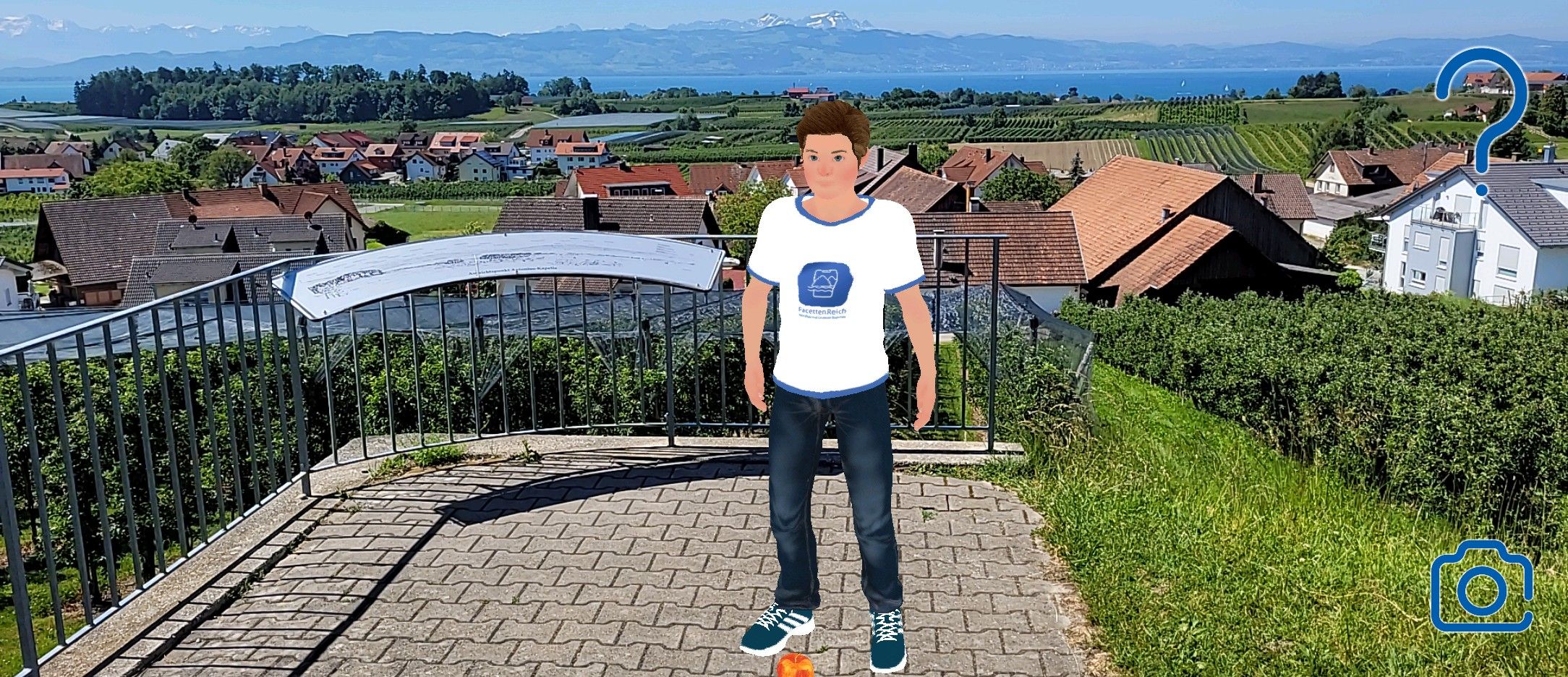 Aussichtspunkt Antoniuskapelle in Selmnau. Im Hitergrund ist der Bodensee und die Bergwelt zu sehen. Inmitten des Aussichtspunkt steht der Avatar der App Facettenreich.