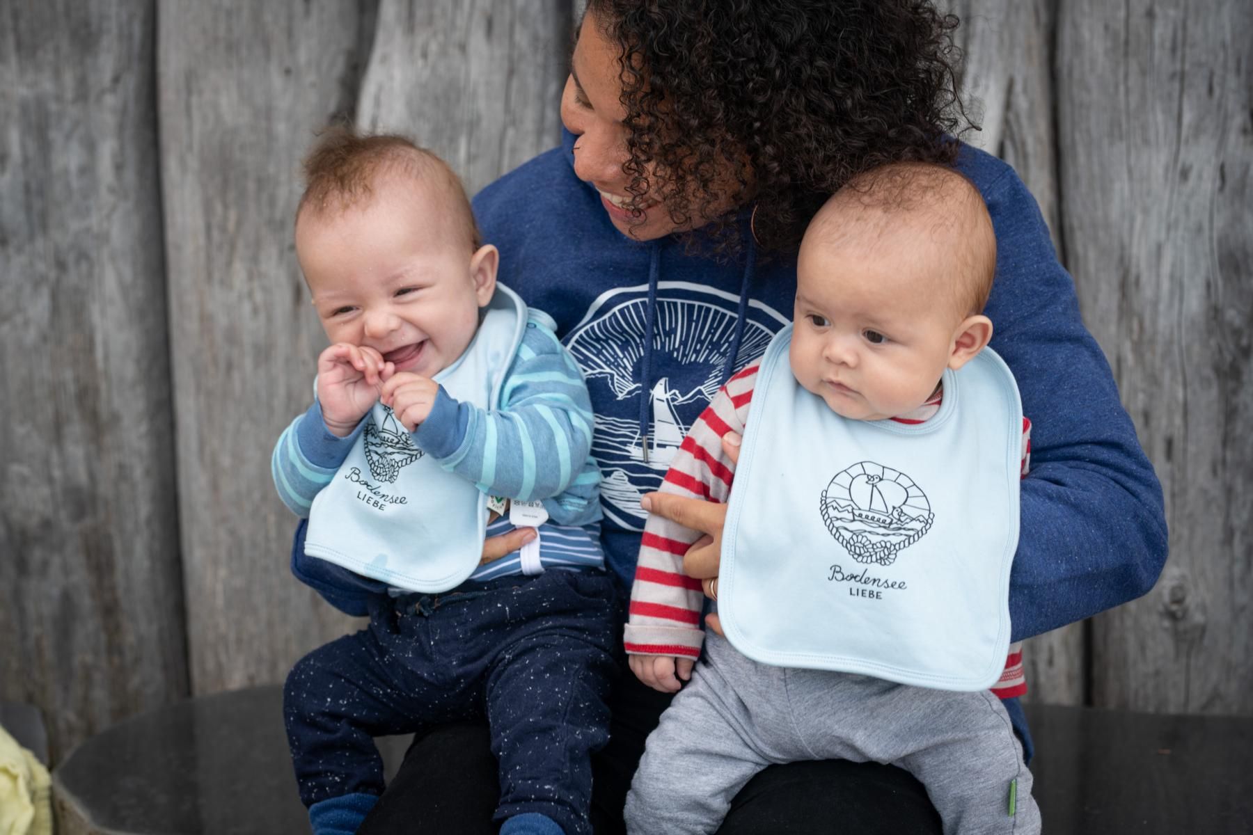 Eine Frau mit zwei Babys auf dem Arm. Die Babys haben von Bodenseeliebe Baby- Lätzchen an.
