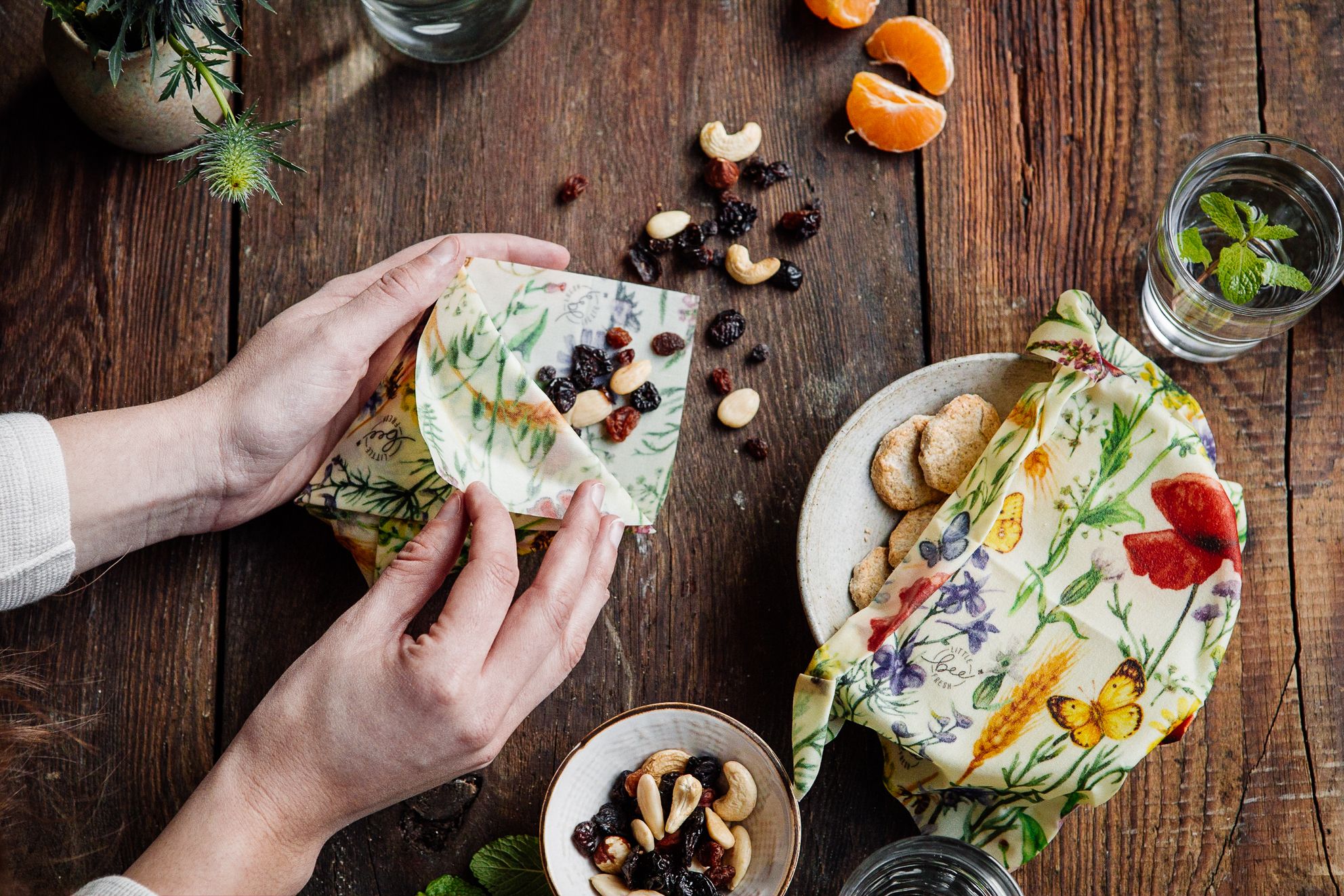 Little Bee Fresh, 100% Bio-Bienenwachstücher. Ein Biowachstuch denkt Lebensmittel ab. Im Hintergrund Nüsse und Mandarinen auf einem Tisch.
