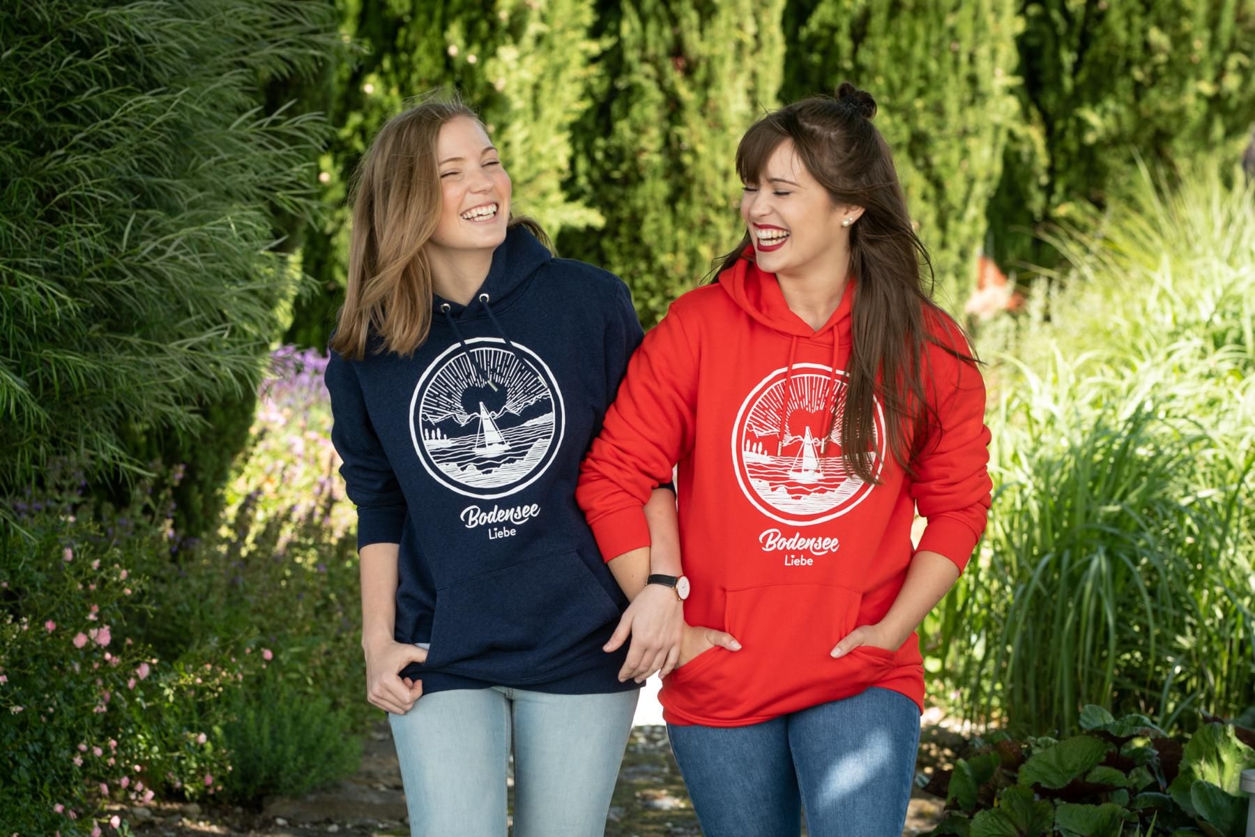 Zwei Frauen die in einem Park laufen, beide haben einen Bodenseeliebe Hoddy an.
