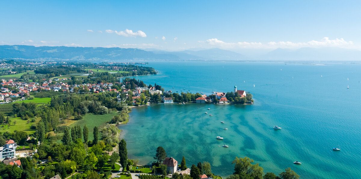 Luftaufnahme Wasserburger Halbinsel Inmitten vom See. Im Hintergrund sieht man die Bergwelt