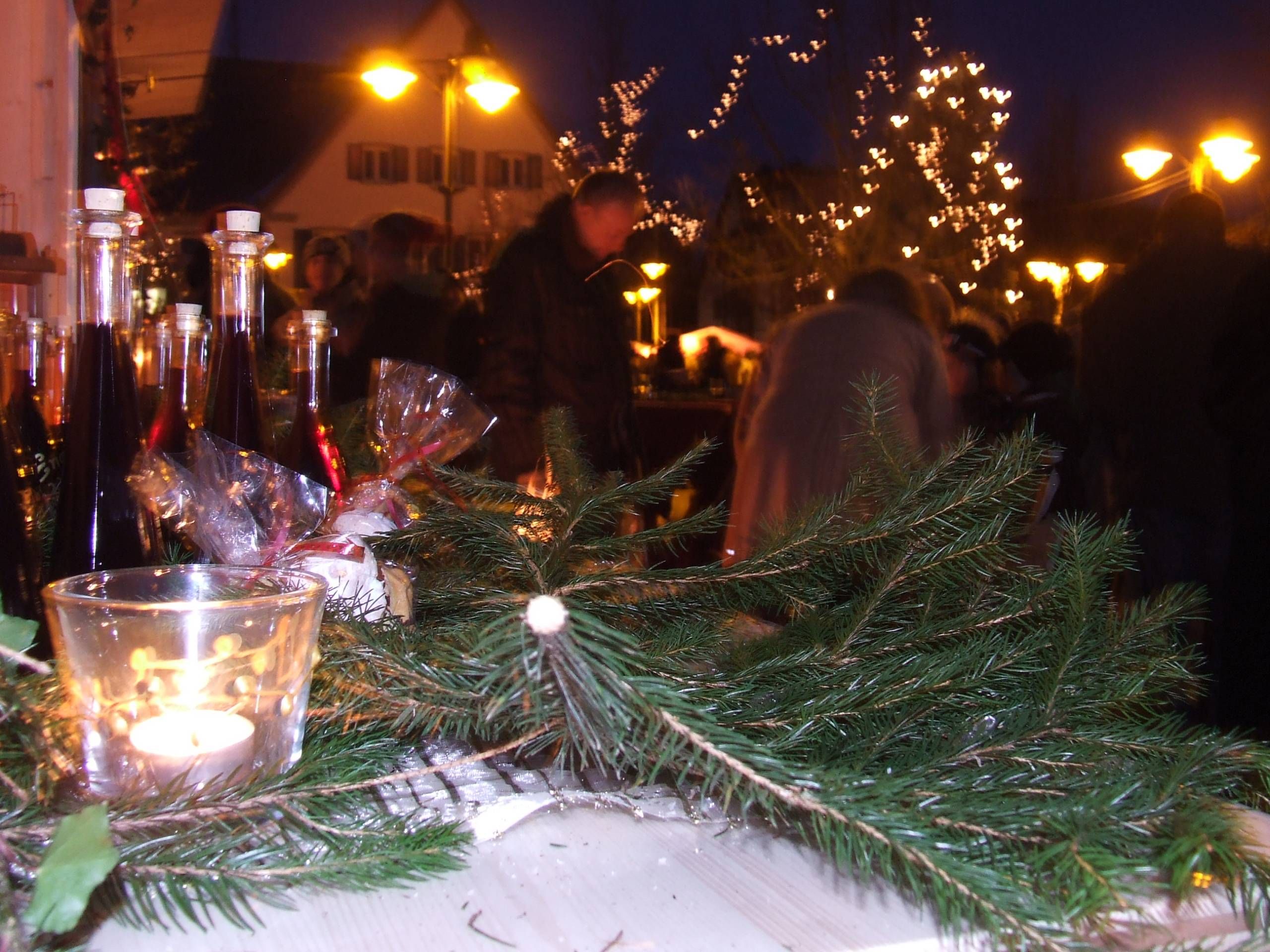 Tannenzweig mit einem Teelicht. Im Hintergrund Likörflaschen.